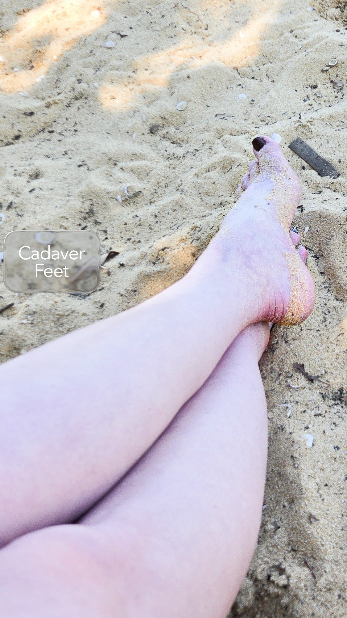 pale feet with dark toe nails resting on a sandy beach
