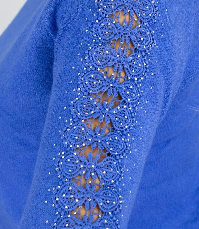 Detailansicht eines blauen Pullovers mit filigraner Spitze und Strasssteinen an den Ärmeln.