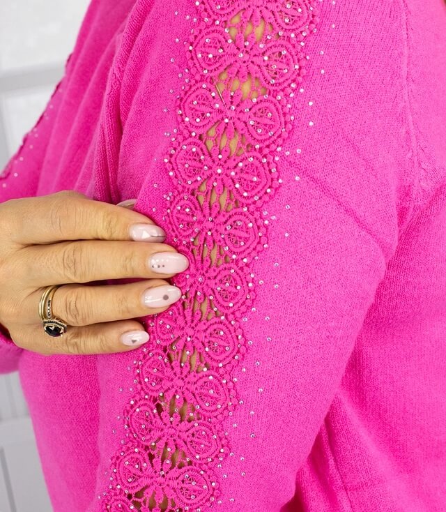 Detailansicht eines pinkfarbenen Pullovers mit dekorativen, bestickten Ärmeln und Glitzerakzenten.