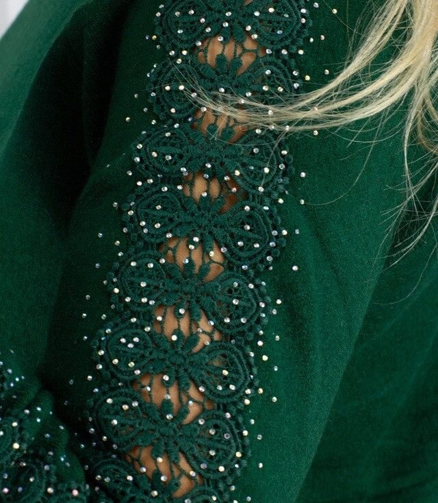 Detailansicht eines grünen Oberteils mit Spitzenbesatz und Glitzersteinchen an den Ärmeln.