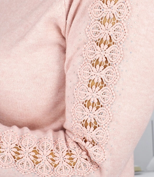 Detailansicht eines rosa Pullovers mit Spitzenbesatz an den Ärmeln für einen eleganten Look.