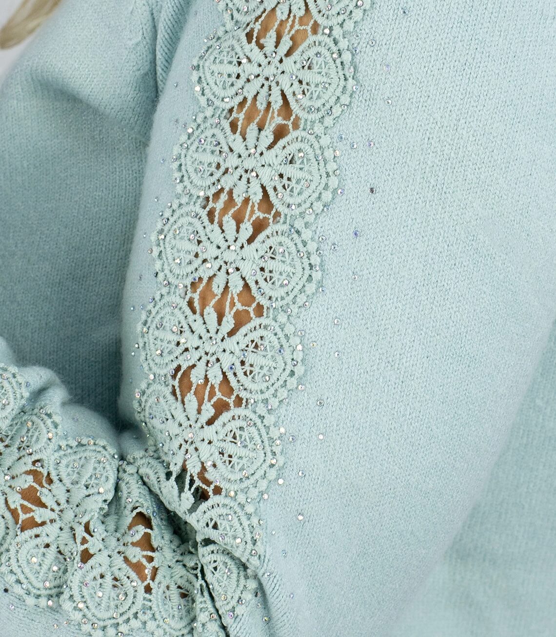 Detailansicht eines mintgrünen Pullovers mit Spitzenborte und Strasssteinen an den Ärmelöffnungen.