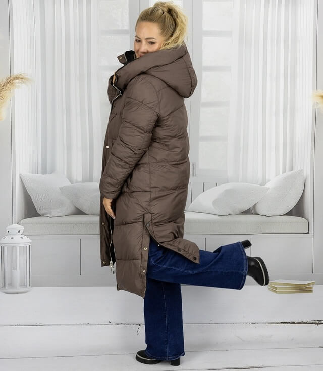 Dunkelbrauner Kapuzenmantel in Langform, getragen von einer Frau in einem hellen Raum.