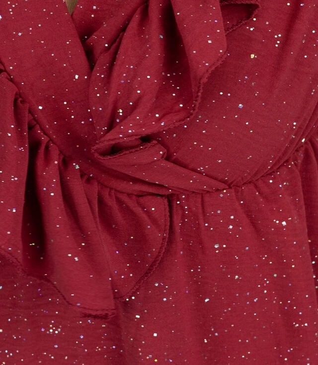 Detailbild eines rotes Kleides mit schimmernden Glitzerpunkten und Raffung im oberen Bereich.