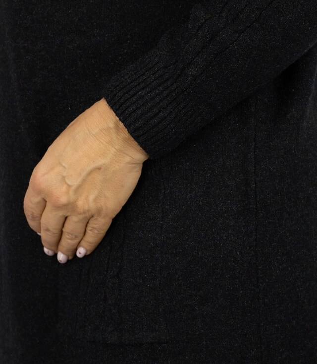 Detailansicht des Strickkleids mit Hand, die den darunterliegenden Stoff und die Taschen zeigt.