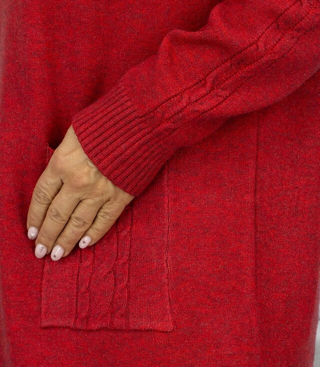 Detailaufnahme eines roten Strickkleides mit sichtbarem Zopf-Muster und seitlicher Tasche.