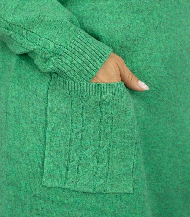 Detailansicht des grünen Strickkleids mit einer großen, strukturierten Tasche auf der Vorderseite.