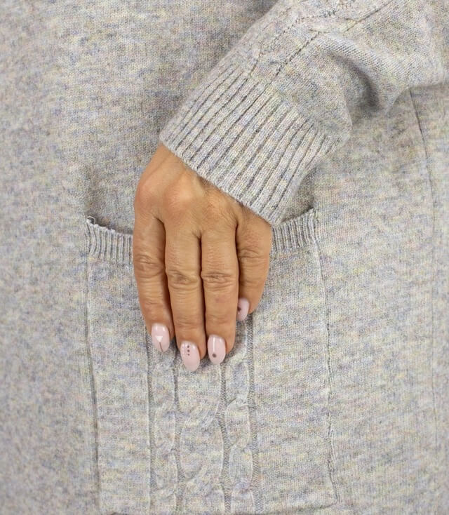 Detailansicht des grauen Strickkleids mit einer Hand, die in die seitliche Tasche greift.