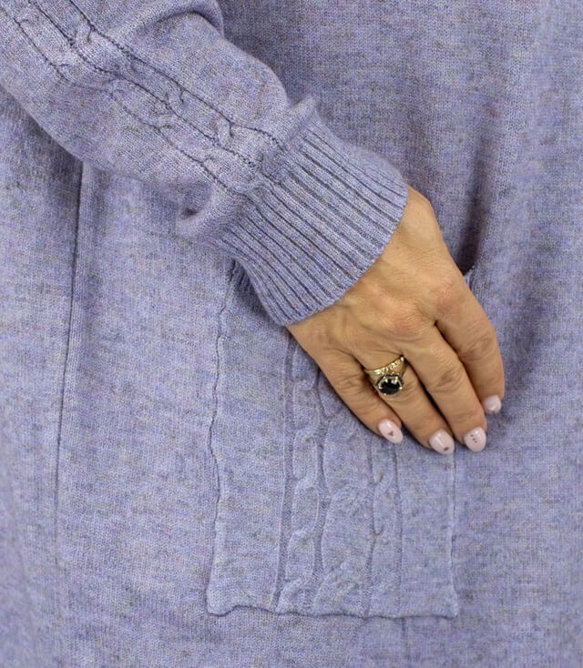 Detailansicht des Strickkleids mit Zopfmuster und seitlicher Tasche in sanften Lilatönen.
