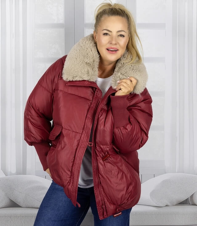 Frau trägt rote Winterjacke mit großem, weichem Kragen vor hellen Fenstern.