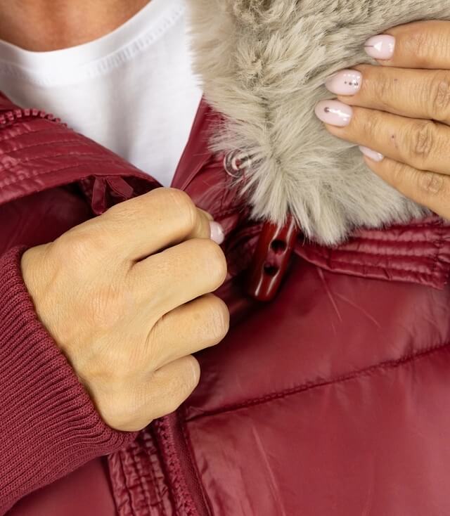 Detailansicht der burgunderfarbenen Jacke mit abnehmbarem Fellkragen und Hand, die den Reißverschluss schließt.