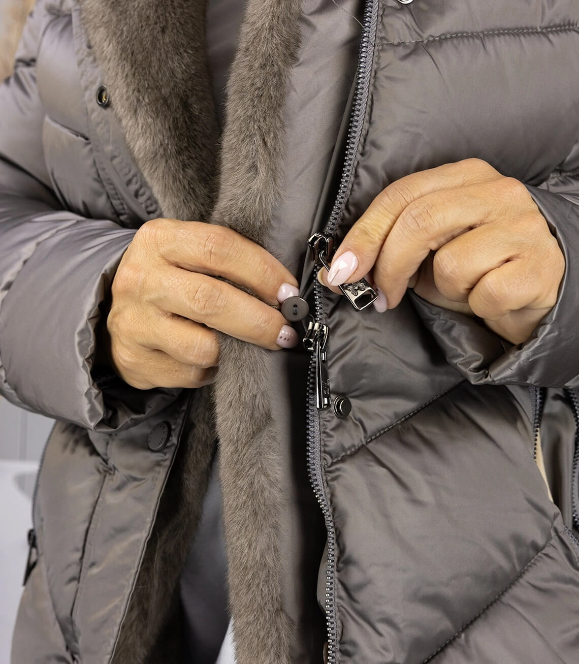 Detailansicht einer Person, die den Reißverschluss einer grauen Winterjacke öffnet.