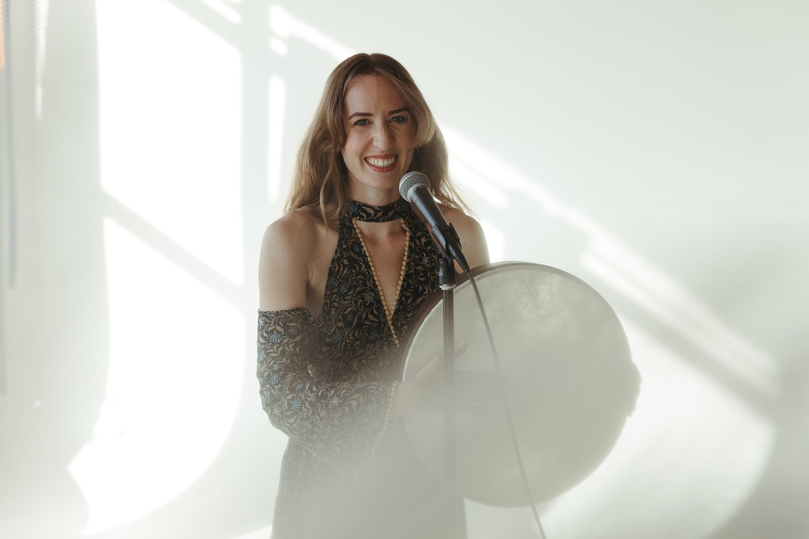abby ilardi smiles in front of a microphone holding a drum
