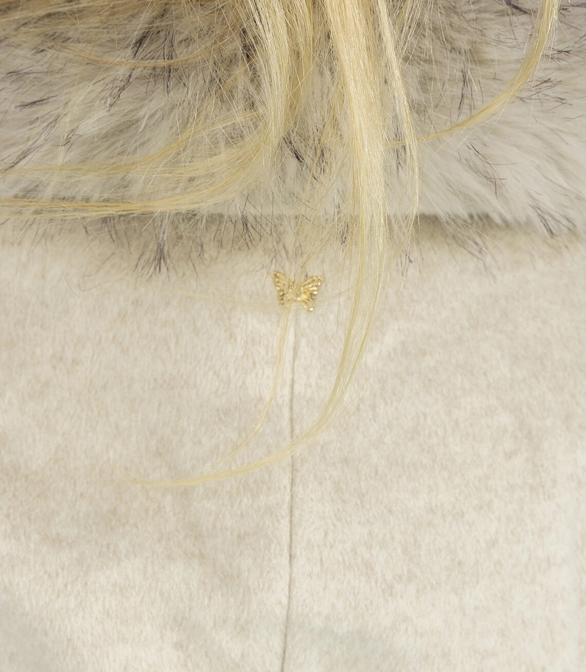 Detailaufnahme eines goldenen Schmetterlingsanhängers auf einem hellen, samtigen Stoff.