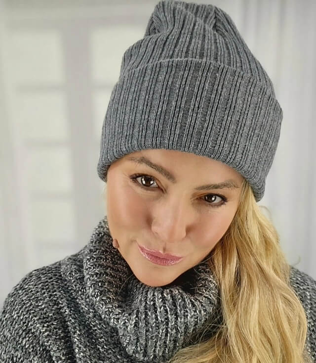 Frau mit blonden Haaren trägt eine graue, gestreifte Mütze und einen gemütlichen Pullover.