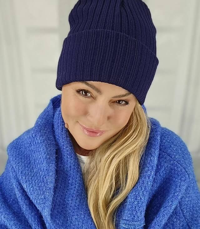 Model trägt eine dunkelblaue Mütze mit Rippenmuster, eingekuschelt in einem blauen Oberteil.