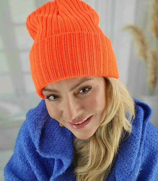 Frau trägt eine leuchtend orange Mütze mit Rippstrickmuster und blickt nach unten.