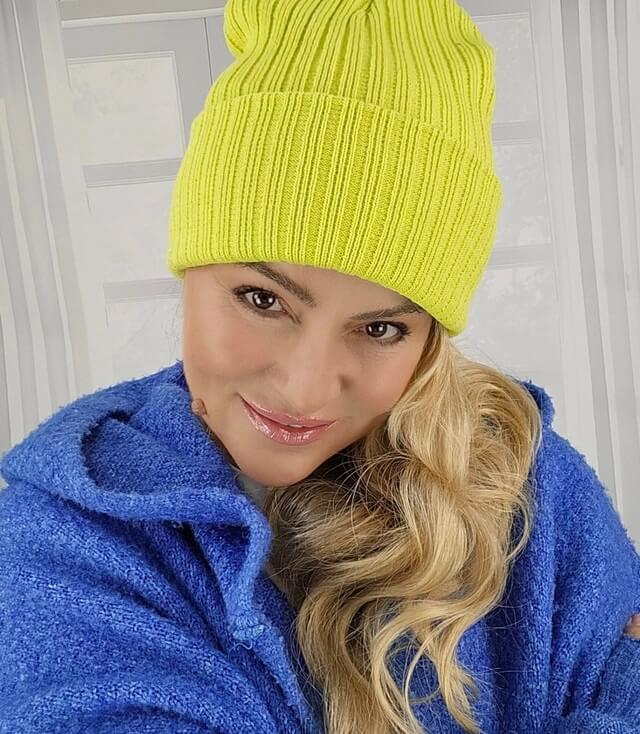 Frau trägt eine leuchtend gelbe Mütze und eine blaue Jacke, lächelt freundlich in die Kamera.