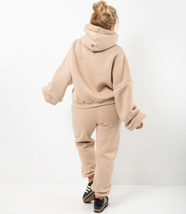 Dame in beigem Jogginganzug mit Kapuze, lockerer Passform und langen Ärmeln, von hinten fotografiert.