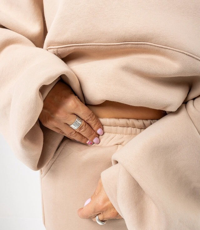 Detailansicht der gemütlichen, beigen Sweatshirt-Hose mit elastischem Bund und lässigen, weiten Ärmeln.