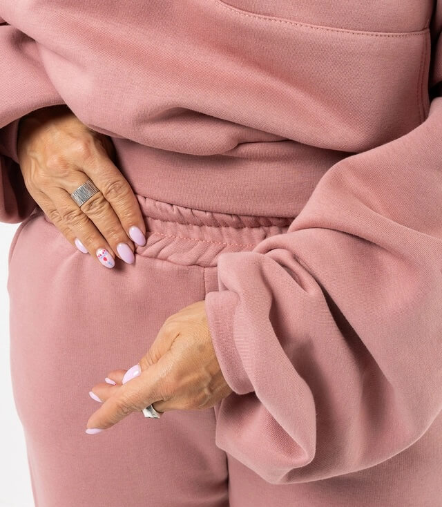 Detailaufnahme der Ärmel und Taille eines rosa Sweat-Outfits mit elastischem Bund und lässigem Schnitt.