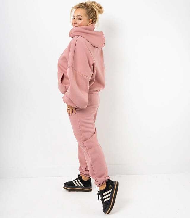 Bild einer Frau in einem rosa Jogginganzug mit Kapuze, kombiniert mit sportlichen Sneakers.