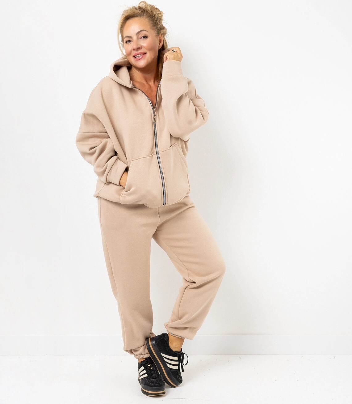 Beigefarbene Kapuzenjacke und Jogginghose mit seitlichen Taschen, entspannter Look und sportlichen Sneakers.