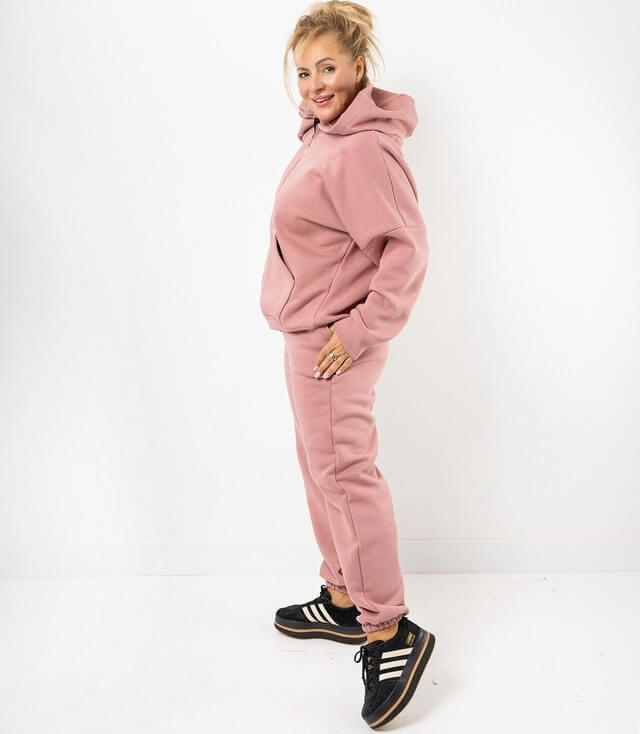 Freizeitanzug mit Kapuze, seitlicher Tasche und samtiger Oberfläche, kombiniert mit schwarzen Sneakers.