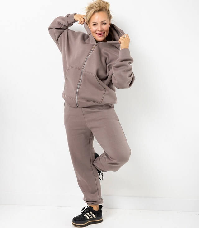 Modischer, bequeme Kapuzen Jacke und Jogginghose in braun, entspannt getragen von einer lächelnden Frau.