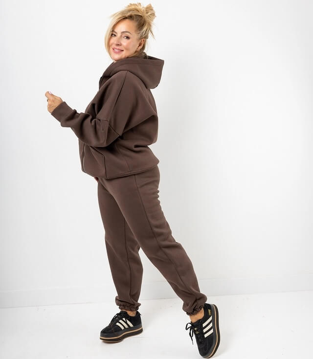 Frau trägt braune Sweatjacke und passende Jogginghose, sportliche Schuhe mit Streifen.