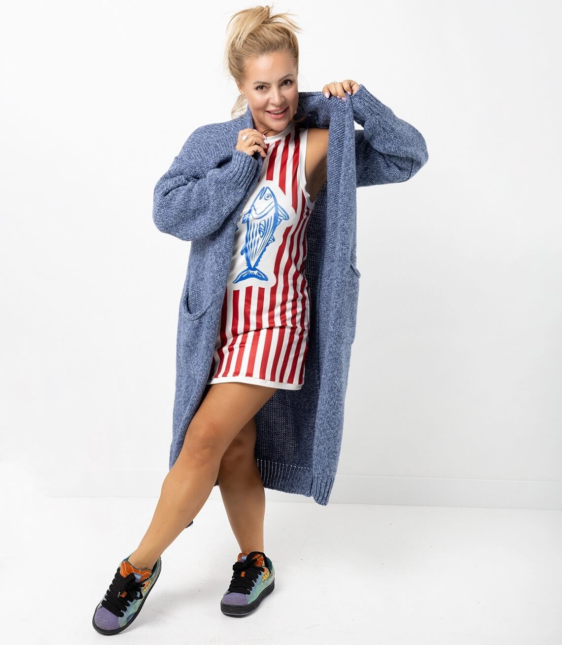 Model trägt einen langen blau gestrickten Cardigan über einem rot-gestreiften Kleid mit Fischmotiv.