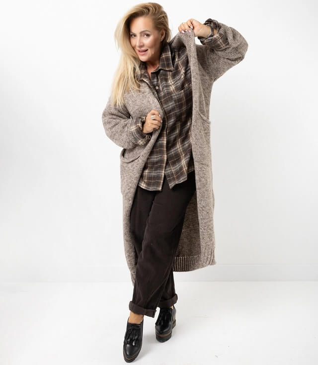 Model zeigt lässigen Look mit einer offenen, braunen Strickjacke, Karobluse und dunklen Hosen.