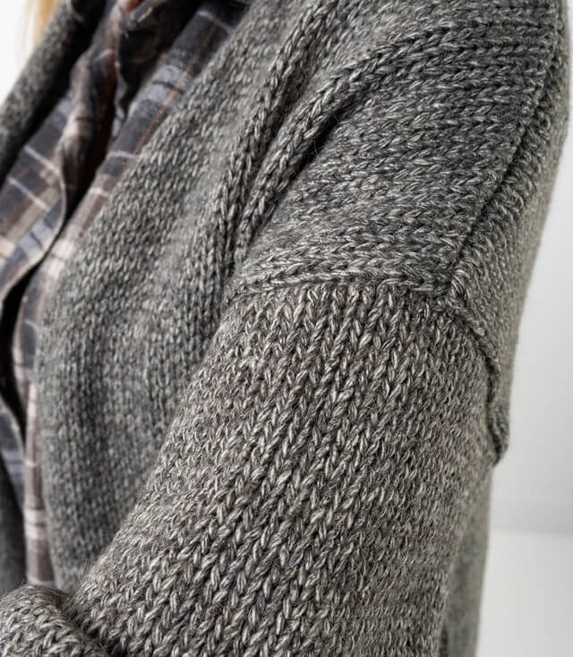 Detailansicht eines grauen Strickcardigans mit strukturiertem Muster und weichem Material.