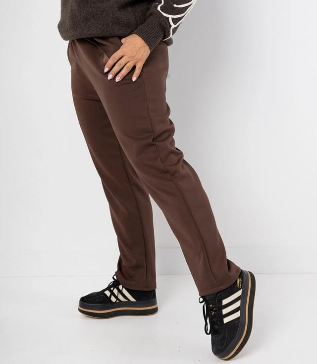 Seitenansicht der schokoladenbraunen Hose mit schmalem Schnitt und sportlichen Sneakern in schwarz-weiß.