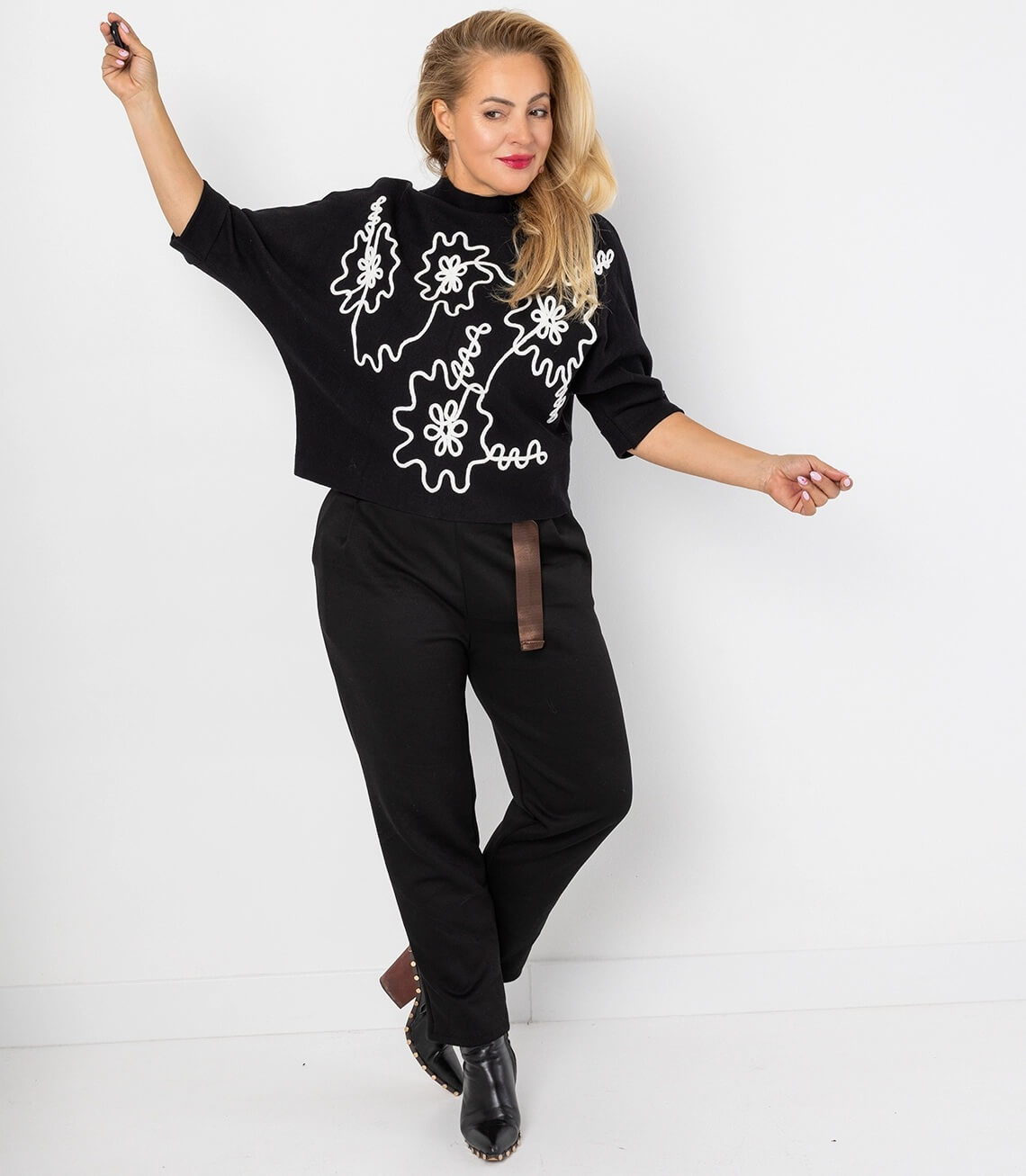 Dame in schwarzer Sweathose mit Gürtel und stylischem Oberteil, lässiger Look.