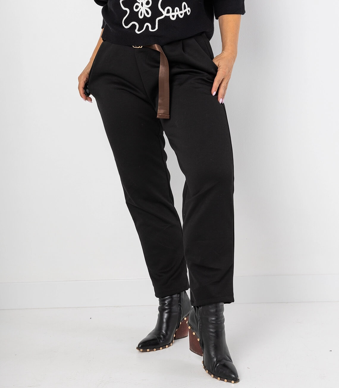 Schwarze Stretch-Hose mit schmalem Schnitt, seitlichen Taschen und dekorativem Gürtel.