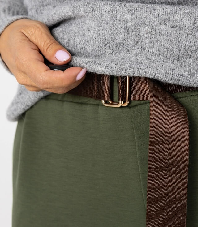 Detailansicht eines Gürtels an der Hose, der mit einer goldfarbigen Schnalle befestigt ist.