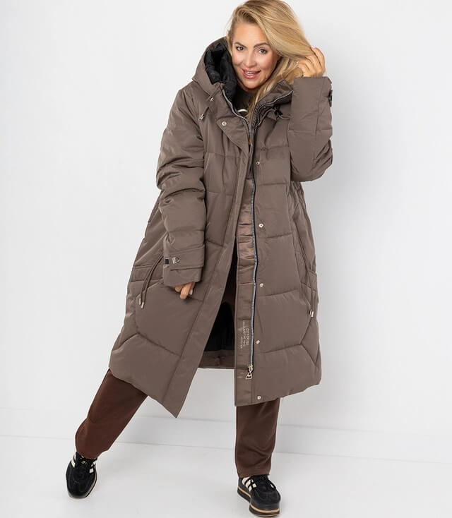 Daunenjacke mit Kapuze, langem Schnitt und seitlichen Taschen, getragen von Model vor neutralem Hintergrund.