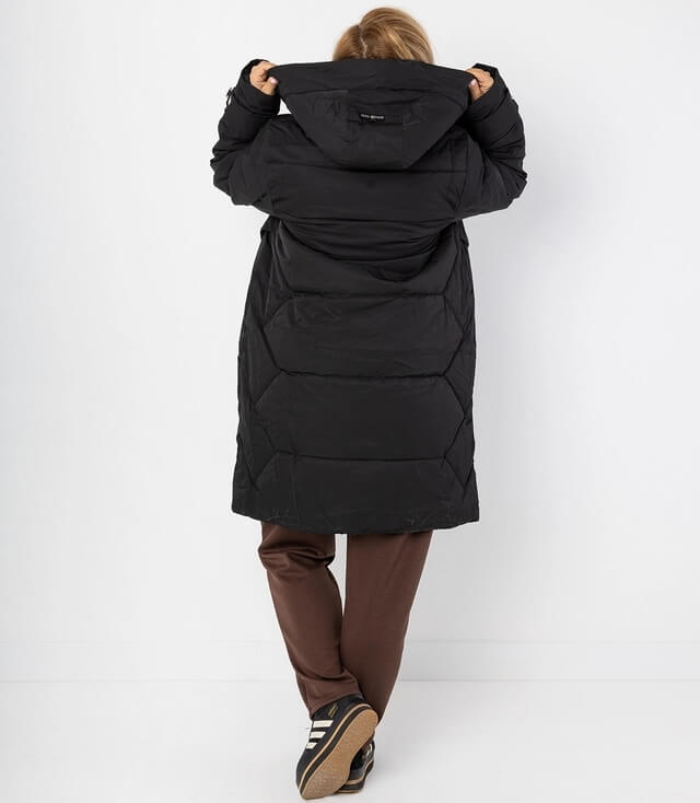 Frau von hinten in einer langen, schwarzen Winterjacke mit Kapuze und sportlichen Schuhen.