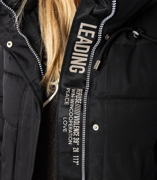 Detailansicht der schwarzen Jacke mit markantem Reißverschluss und Schriftzügen wie LEADING und PEACE.