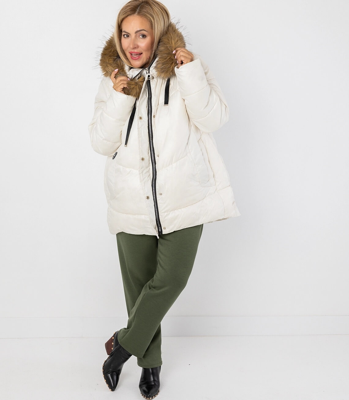 Modische weiße Winterjacke mit Kapuze und Fellkragen, kombiniert mit grüner Hose und schwarzen Schuhen.