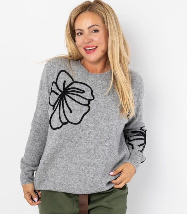 Gemütlicher grauer Pullover mit floralen Schwarz-Stickereien auf den Ärmeln, ideal für Freizeitlooks.