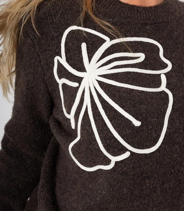 Dunkelbrauner Pullover mit einem großen, weißen Blumenmuster auf der Vorderseite.