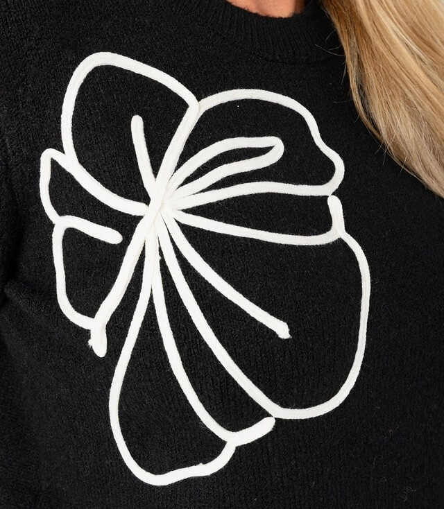 Schwarzer Pullover mit großem weißen Blumenmotiv auf der Vorderseite.