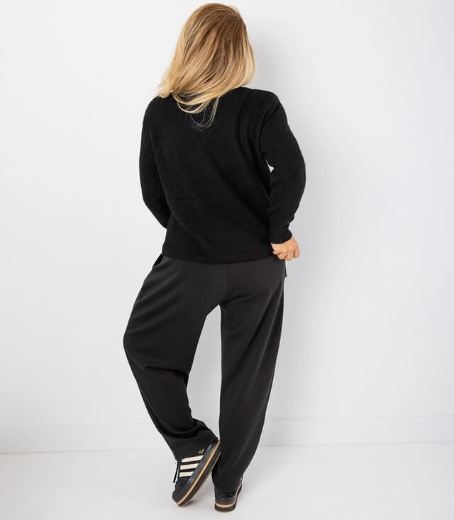 Rückansicht einer Person in einem schwarzen Pullover und lässigen, weiten schwarzen Hosen.