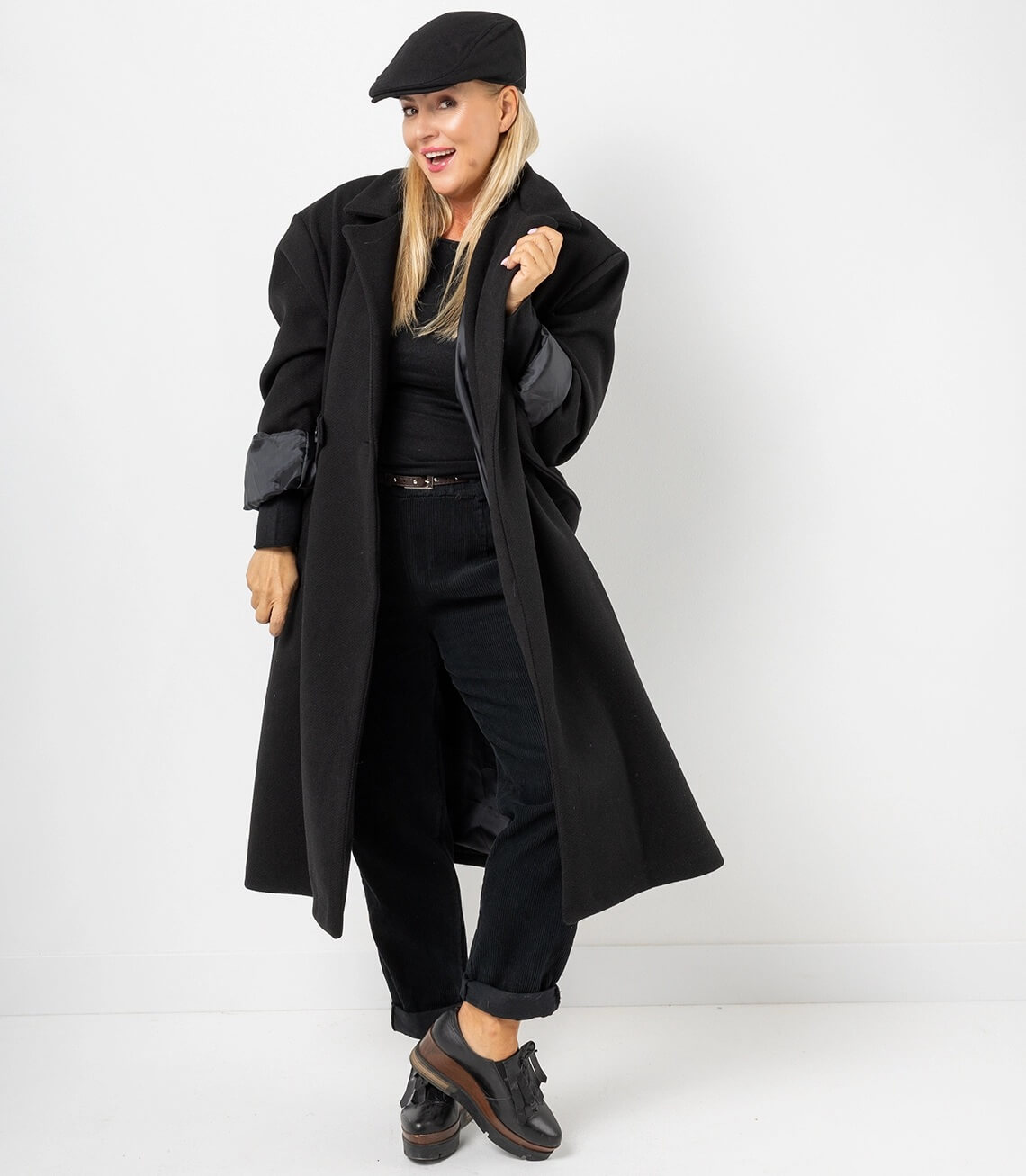 Damen Oversize Trenchcoat großer, offener Kragen und ein kontrastierendes Satinfutter,  in schwarz, lässig getragen mit Cap, lockerer Passform und elegantem Look.