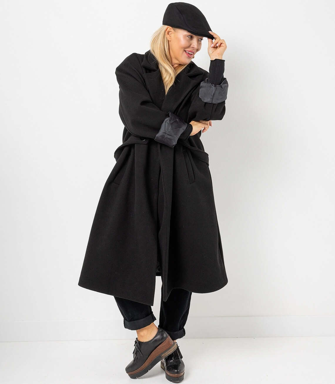 Damen Mantel in Schwarz mit breiten Ärmeln, kombiniert mit einer Schirmmütze und lässiger Hose.