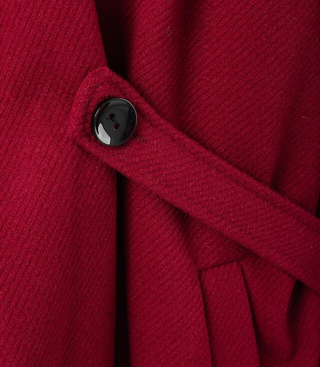 Detailansicht eines roten Mantels mit Knopf und Taillengürtel für eleganten Look.