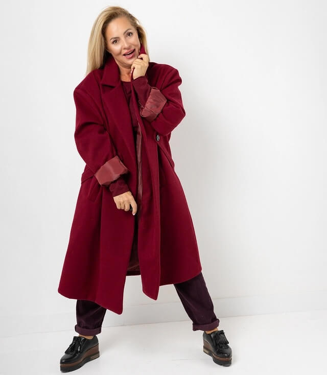 Stylischer burdeauxroter Mantel in Übergröße, getragen von einer Frau, lächelt vor weißem Hintergrund.