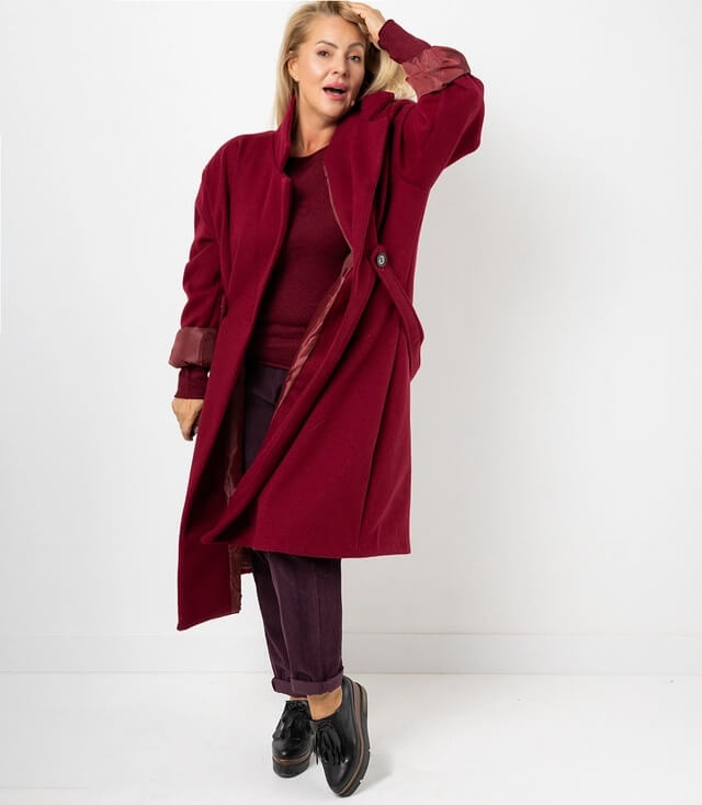 Frau in bordeauxrotem Mantel mit Knopf, kombiniert mit burgunderfarbener Kleidung und schwarzen Schuhen.